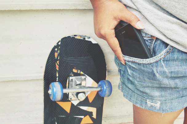 Smart phone in jeans pocket with skateboard - 写真・画像