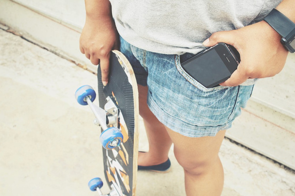 Smart phone in jeans pocket with skateboard - Foto, afbeelding