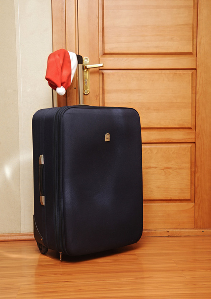 Suitcase and santa hat against a wooden door. - Фото, зображення