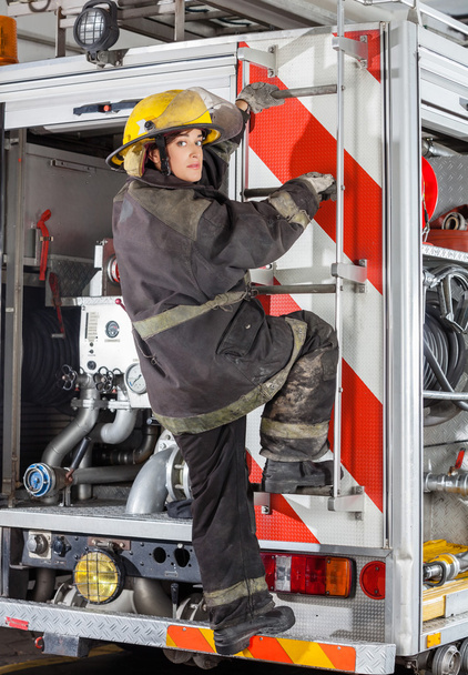 Firewoman Climbing Truck At Fire Station - Foto, afbeelding