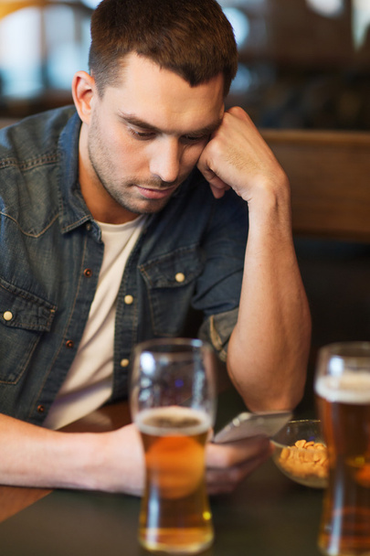man with smartphone drinking beer at bar - Фото, изображение