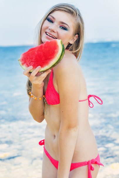 Beauty girl is wearing red swimsuit eating watermelon - Fotó, kép