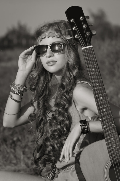 Молодая хиппи девушка на летнем поле со своей гитарой
 - Фото, изображение