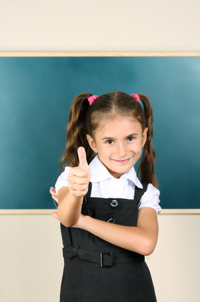 Beautiful little girl standing near blackboard in the classroom - Фото, изображение