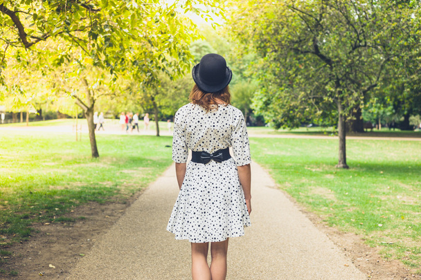 Woman wearing hat and dress walking in park - Fotoğraf, Görsel