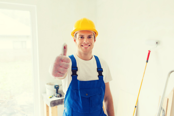smiling young builder in hardhat showing thumbs up - Fotoğraf, Görsel