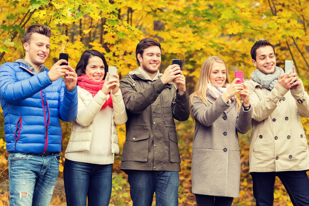 amici sorridenti con gli smartphone nel parco cittadino
 - Foto, immagini