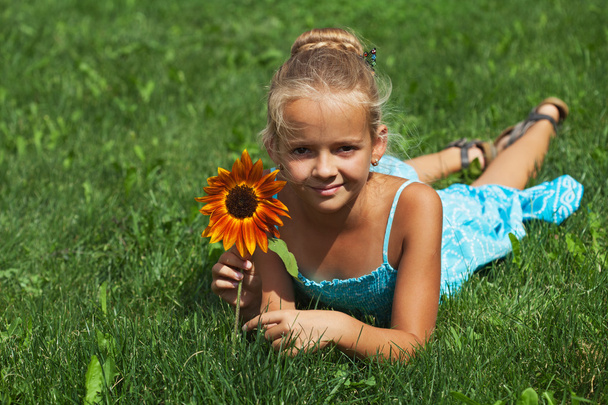 Маленька дівчинка лежить на траві з квіткою
 - Фото, зображення
