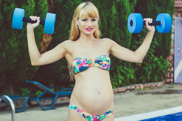 Pregnant girl is doing sport with dumbbells near swimming pool - Fotoğraf, Görsel