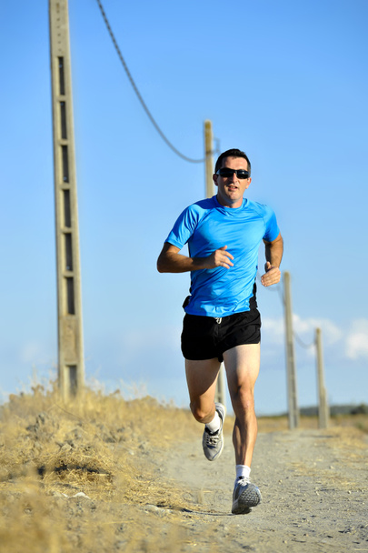 Sportler mit Sonnenbrille läuft mit Stromleitungsmasten auf Landpartie - Foto, Bild