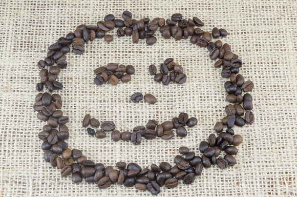 Smileygezicht gemaakt volledig uit koffie korrels geplaatst op koffie - Foto, afbeelding