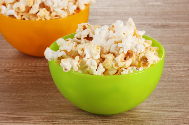 Popcorn in bright plastic bowls on wooden table - Photo, image