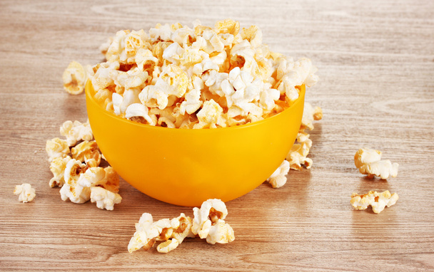 Popcorn in bright plastic bowl on wooden table - Фото, зображення