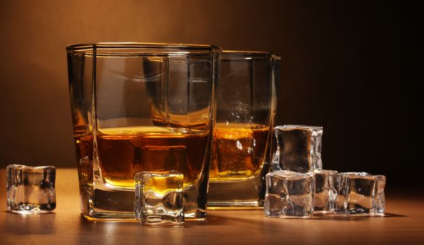 Two glasses of scotch whiskey and ice on wooden table on brown background - Foto, imagen