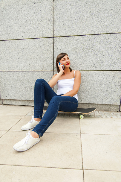 Young girl siting on skateboard in the city talking by phone nea - Fotografie, Obrázek