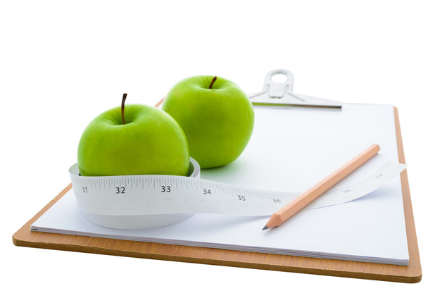 Measuring tape wrapped around a green apple and clipboard - Photo, Image