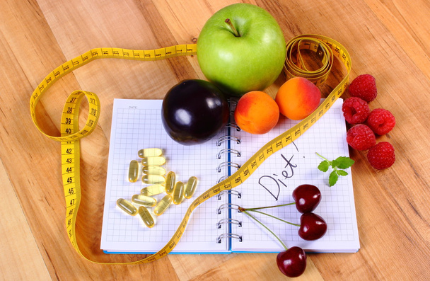 Fruits, tablets supplements and centimeter with notebook, slimming and healthy food - Photo, Image