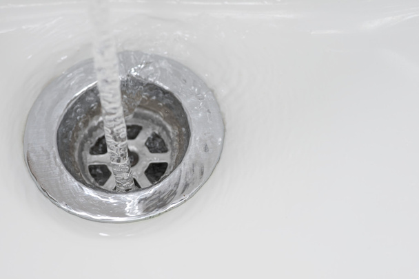 Közelkép a csap víz áramlik rozsdamentes leeresztő háttér fehér mosdó - Fotó, kép