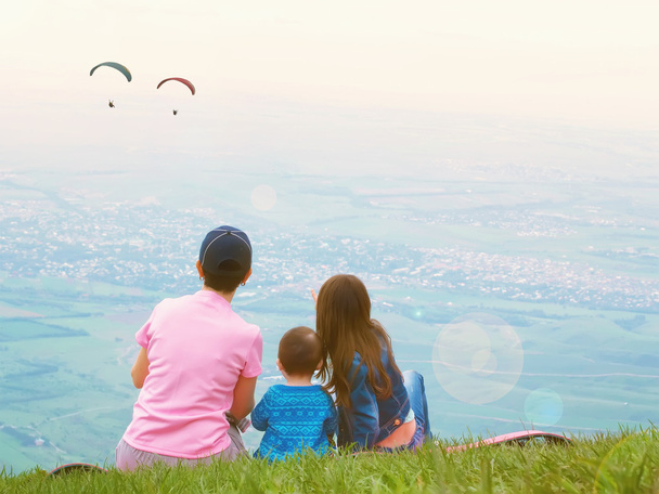 Portrait of family mother brother and sister together sitting in nature look at paraglider - Photo, Image