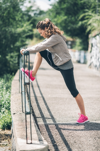An athletic woman in profile stretching out against guardrail - Photo, image