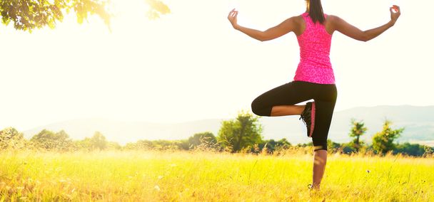 Pratik Yoga bir çayır mercek parlaması ile günbatımı, görüntü üzerinde genç atletik kadın - Fotoğraf, Görsel