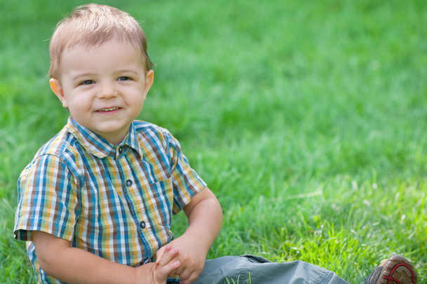 Closeup portret van een glimlachende jongen tegen het groene gras - Foto, afbeelding