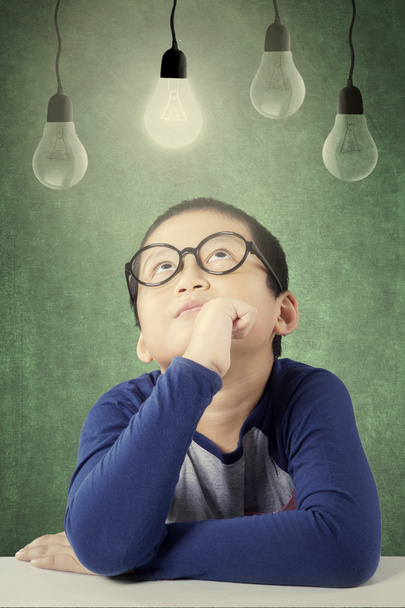 Male primary school student sitting under light bulb - Foto, afbeelding