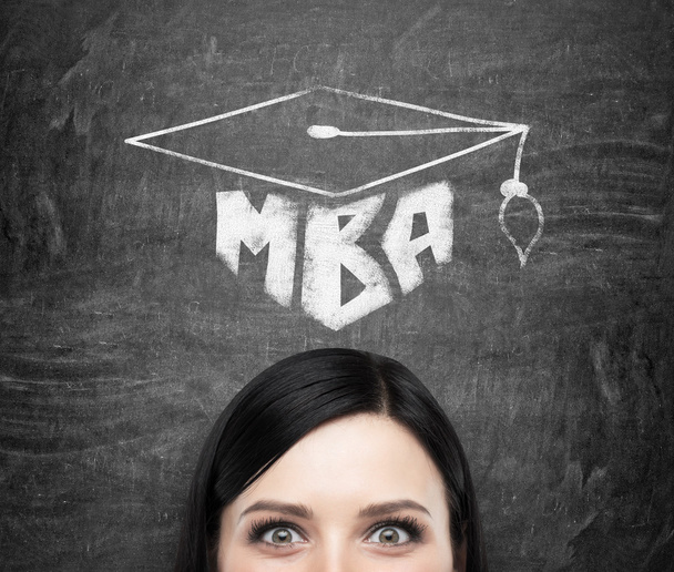 A head of young brunette lady who is thinking about MBA degree. Drawn a graduation hat on the black chalkboard background . - 写真・画像