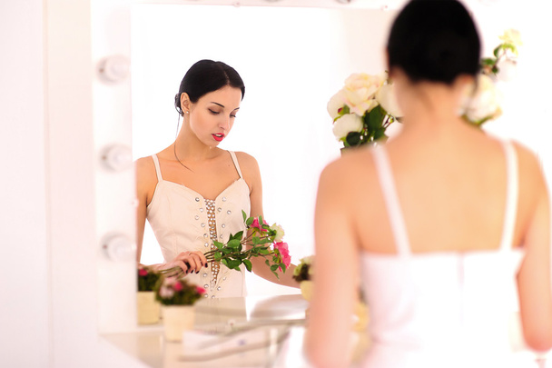 Kaunis nuori ballerina seisoo peiliä vasten ja katselee hänen kukkia
 - Valokuva, kuva
