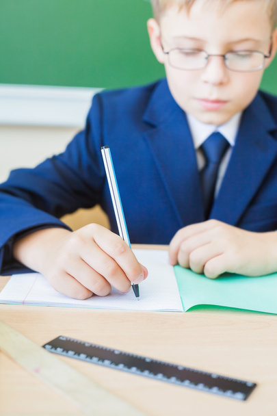 schoolboy sitting at desk at school and writing to notebook - Foto, Imagen