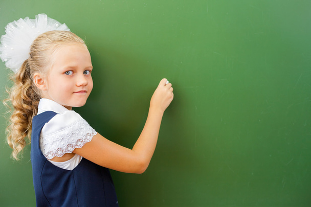 First grade schoolgirl wrote on blackboard with chalk at classroom - Фото, изображение