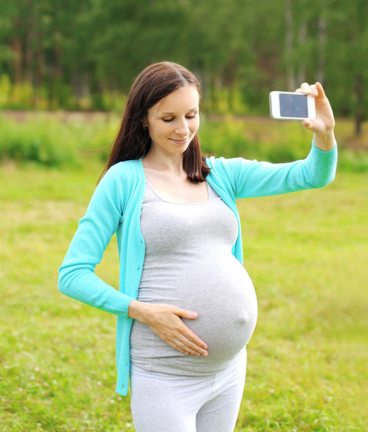 Happy young pregnant woman makes self-portrait on the smartphone - Fotó, kép