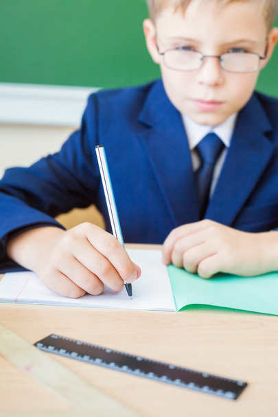 schoolboy sitting at desk at school and writing to notebook - Фото, изображение