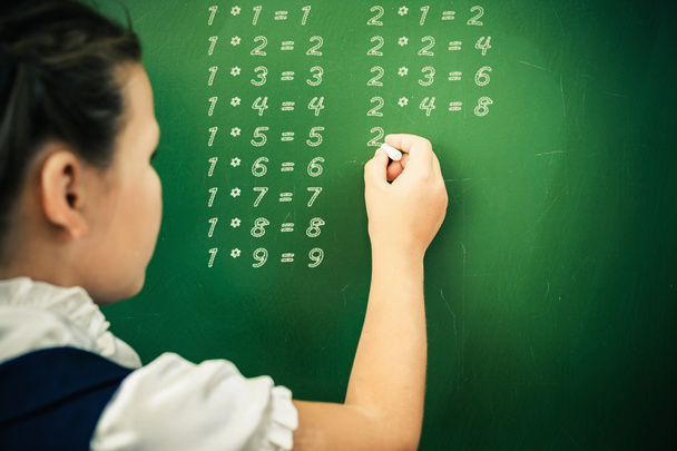 First grade schoolgirl wrote multiplication table on blackboard with chalk - Фото, зображення