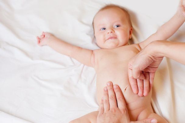 Mother makes baby massage with happy newborn at white bed - Valokuva, kuva
