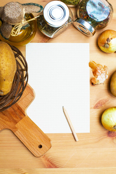 Papier, ołówek, dzban oliwy z oliwek, ziemniaki, cebula, deska do krojenia i przyprawy - Zdjęcie, obraz