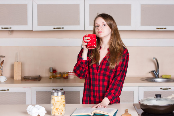 Tyttö, jolla on pitkät hiukset punaisessa paidassa. keittiö cup kätensä
 - Valokuva, kuva