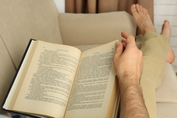 Молодий чоловік читає книгу на дивані крупним планом
 - Фото, зображення