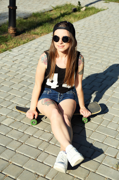 Beautiful tattooed girl with skateboard, outdoors - Фото, изображение