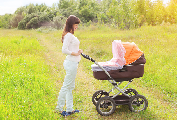 glückliche junge Mutter spaziert mit Kinderwagen im Freien auf dem na - Foto, Bild