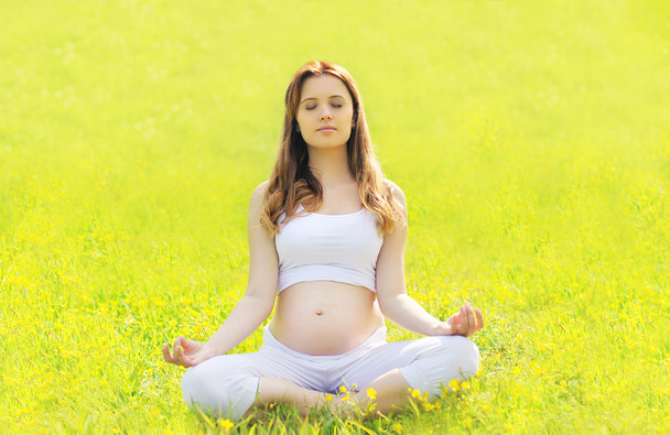 Pregnant woman sitting on the grass doing yoga exercise in sunny - Photo, Image