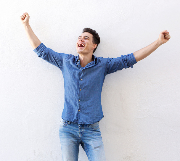 fröhlicher junger Mann mit erhobenen Armen feiert - Foto, Bild