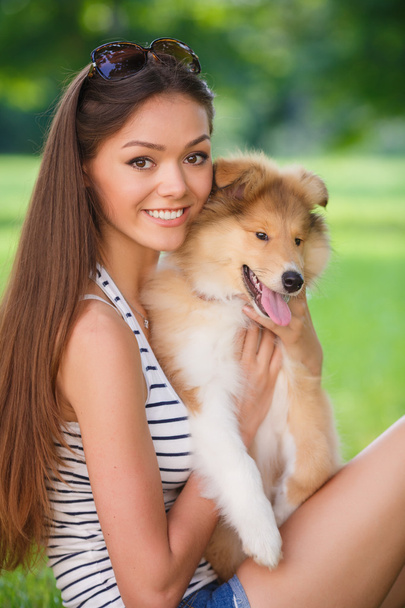 Young beautiful woman playing in a green park with a small puppy collie - Фото, изображение
