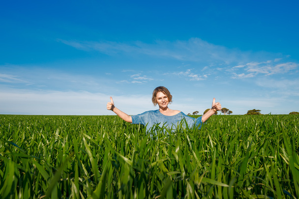 Mujer mostrando los pulgares hacia arriba gesto en el campo verde
 - Foto, Imagen