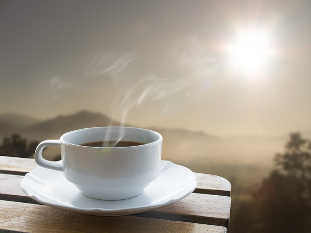 Tasse Kaffee und über Holztisch und Sonnenaufgang hinter dem Berg - Foto, Bild