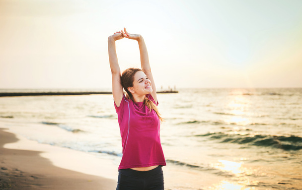 Fitness-urheilumalli hymyilee onnellisia harjoituksia ulkoilun aikana auringonnousun aikana. Kaunis valkoihoinen nainen koulutus ulkona meren rannalla aamulla
 - Valokuva, kuva