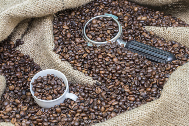 Arm der Kaffeemaschine und Tasse in einem Beutel voller Kaffeebohnen - Foto, Bild