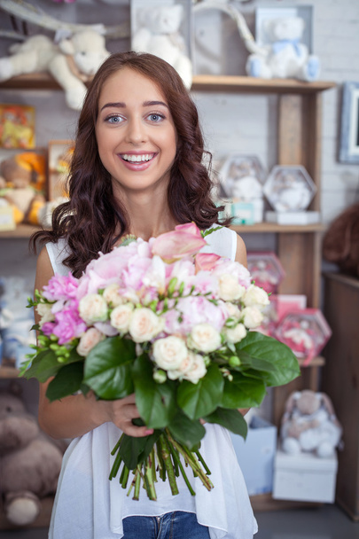 Cheerful young woman is buying bouquet in flower shop - Foto, imagen