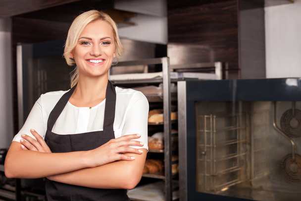 Cheerful young female cook is working in bakery - Foto, imagen