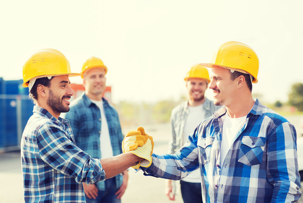 group of smiling builders shaking hands outdoors - Foto, Imagen